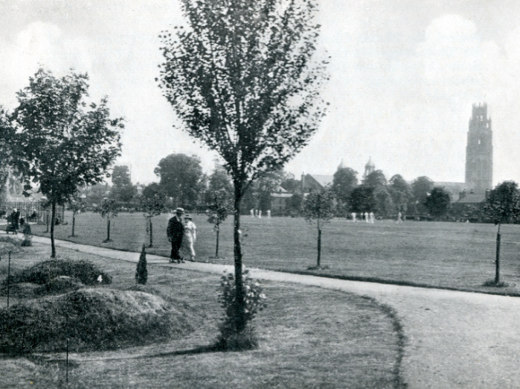 A black and white photograph of Central Park. A couple are strolling along the path, Boston Stump can be seen in the distance.